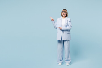 Full body successful employee business woman 50s wearing classic suit glasses formal clothes point index finger aside on area mock up isolated on plain pastel blue background. Lifestyle work concept.