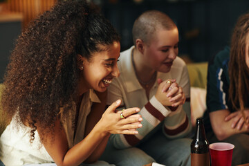 Multiracial group of friends enjoying conversation in a cozy indoor environment, sharing laughter while sitting close together and engaging in friendly interaction