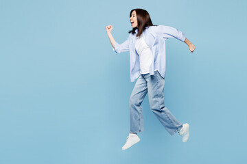 Full body side view young Caucasian woman she wears shirt casual clothes jump high run fast hurry up be in rush isolated on plain pastel light blue cyan background studio portrait. Lifestyle concept.