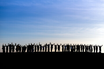 a silhouette of a large group of people standing together with their arms raised against a sky...