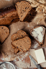 rye bread with raisins, dried apricots, sunflower seeds, caraway seeds, two loaves of bread on a wooden background, flour, sieve, rolling pin, eggs, homemade bread, wheat ears, black bread with butter