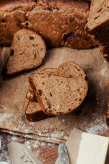 rye bread with raisins, dried apricots, sunflower seeds, caraway seeds, two loaves of bread on a wooden background, flour, sieve, rolling pin, eggs, homemade bread, wheat ears, black bread with butter