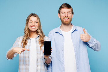 Young couple two friends family man woman wearing shirt casual clothes together hold use mobile cell phone with blank screen area show thumb up isolated on pastel plain light blue background studio.