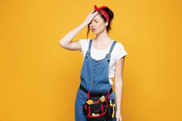 Young employee laborer handyman woman wear overalls belt put hand on face facepalm epic fail gesture isolated on plain yellow background. Instruments for renovation apartment room Repair home concept