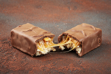 Closeup of chocolate bar with peanuts, caramel and nougat, brown background