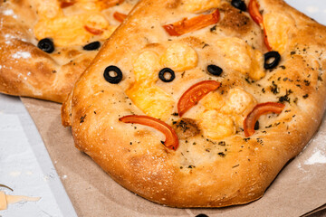focaccia with cheese, olives, olive oil, tomatoes on kraft paper on a light background, next to a cheese grater, a bowl of olives, Italian herbs, Italian pastries, yeast dough