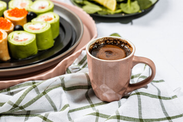 Americano espresso coffee in a small ceramic pink cup on a light background, a white-green serving napkin, healthy food in the background, a salad with spinach and lemon