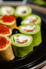 green pancakes rolls with Philadelphia cheese, red fish, red caviar, lemon, olives, pancakes with caviar, spinach, flatlay, Maslenitsa, Japanese rolls, cream cheese with salmon, still life