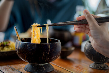 Crop anonymous female with chopsticks eating yummy  noodles and meat in wooden bowl at nodles restaurant.