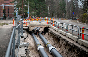 Large black underground pipes being installed in an excavated trench at a construction site,...