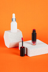 White tube and red spray on light white podiums. White blank unbranded flacons with cosmetology products. Professional concept of skin care on orange background.