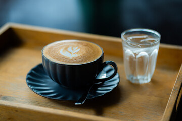 Side view of hot latte coffee with latte art in a black cup on black wooden table