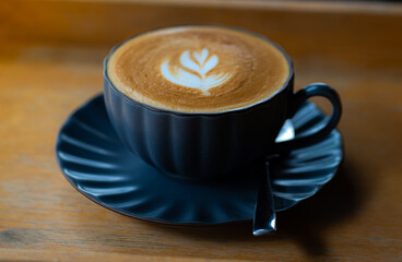 Side view of hot latte coffee with latte art in a black cup on black wooden table, Close up and selective focus.