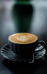 Side view of hot latte coffee with latte art in a black cup on black wooden table