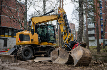 yellow wheeled excavator with a hydraulic grapple attachment at an urban construction site
