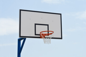 Naklejka premium A basketball hoop with a white backboard and orange rim stands against a light blue sky