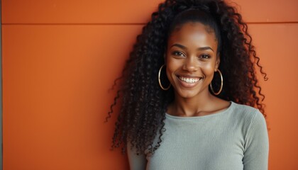 Joyful young African woman with curly hair smiling against an orange backdrop in an outdoor setting