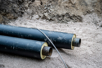 Two large insulated steel pipes lie on a construction site with exposed soil and gravel. 