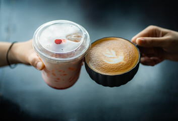 Top view image of  women's hands holding coffee and glass of ice strawberry latte with black wooden table background