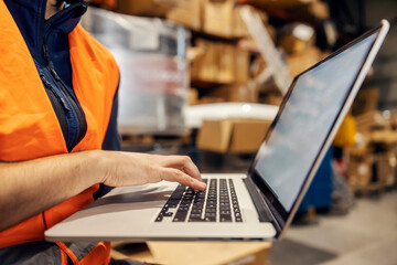 Close up of stock clerk typing on laptop and tracking shipment online.