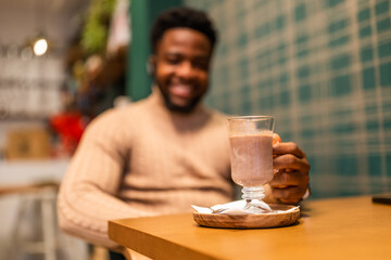 Young black man enjoying hot chocolate in bar. Selective focus on glass with hot chocolate.
