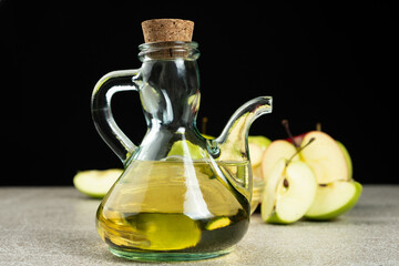 Apple cider vinegar in a glass vinegar bowl among apples