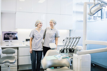 Two women in white hats stand in front of a dental office