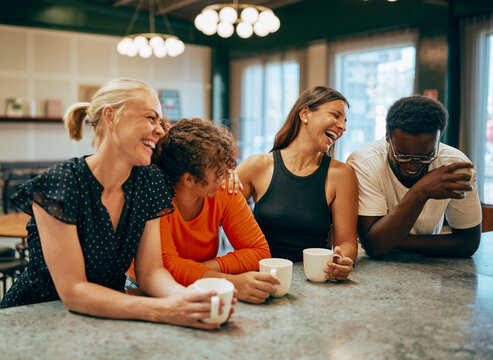 Diverse Group of four Friends Laughing Together at a Coffee Shop. They are wearing casual summer clothes