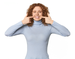 Young Caucasian redhead woman smiles, pointing fingers at mouth.