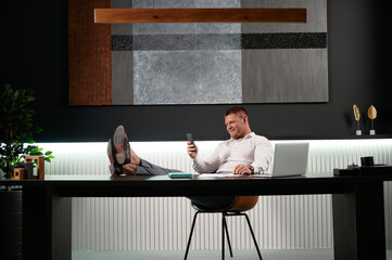 Young man sitting at his desk in the office had his legs draped over it. Working in a relaxed...