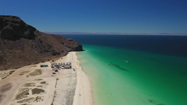 Famous beach Playa el Tecolote. Turquoise water meets a sandy beach under a sunny sky, with a mountain rising in the background. 