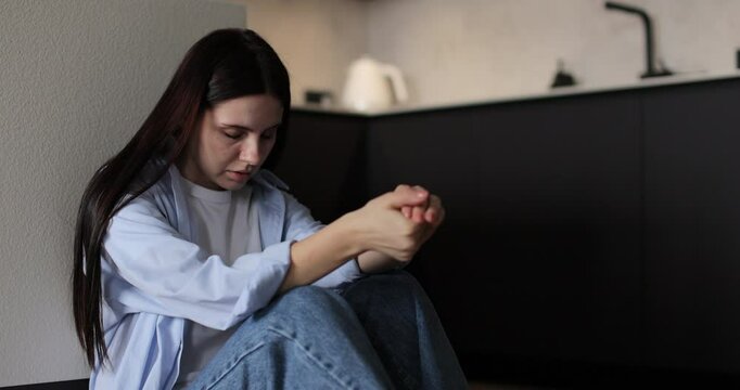 Woman sitting on kitchen floor crying with head in hands. Family problems, stress.