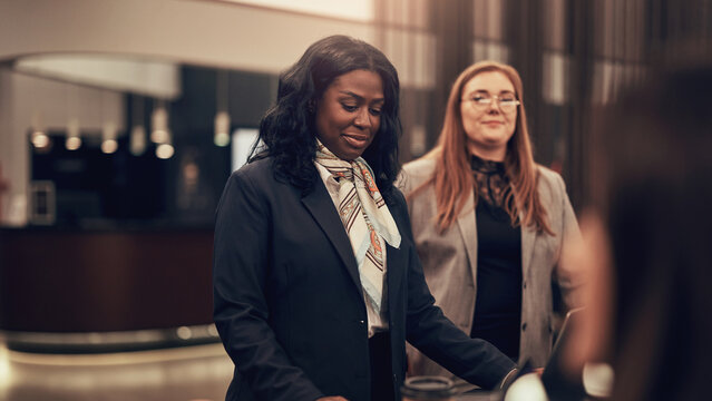 Diverse businesswomen working in the lobby of a hotel during a business trip. They are both wearing blazers