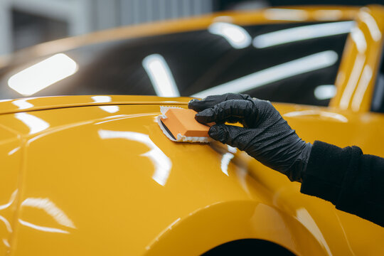 Car detailing worker applying ceramic car coating on yellow car at workshop