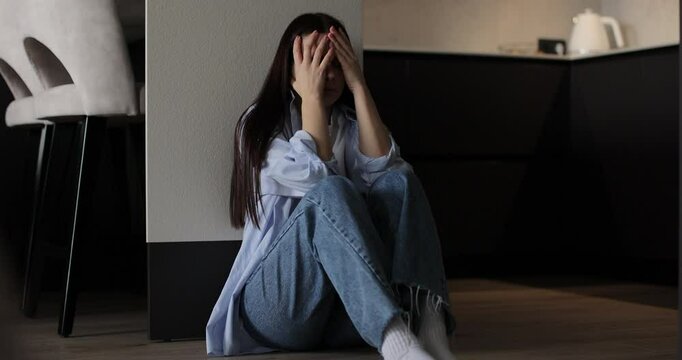 Woman sitting on kitchen floor crying with head in hands. Family problems, stress.