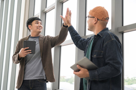 Asian male businessman Tag a friend's hand happy smile Holding a tablet, talking about analytics, innovation, and collaboration. Online business, sales techniques, strategic planning