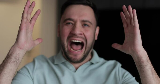 Close up of a young stressed man shouting on living room background. Motions concept. Man's reaction to bad news.