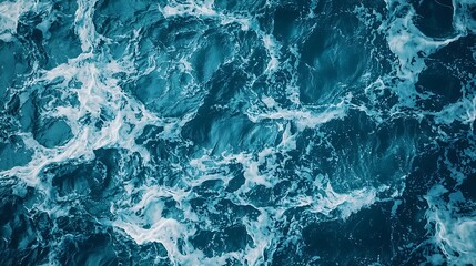 Obraz premium Aerial view of turbulent ocean waters, showcasing swirling patterns and frothy white waves against a deep blue backdrop.