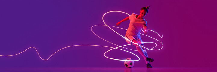 Young female soccer player in sportswear, in mid-stride controlling ball surrounded by vibrant pink neon light streaks against purple background. Concept of sport, competition, tournament, game.