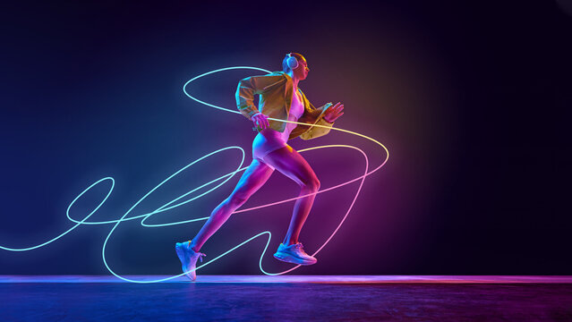 Female runner in sportswear and headphones sprinting, running with neon blue and pink swirls capturing rhythm and intensity against dark gradient background. Concept of sport, health, endurance