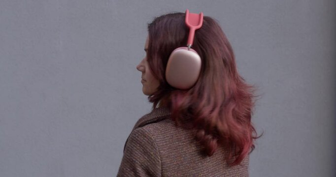A red-haired girl dances to music from headphones, turns and looks at the camera, smiles.