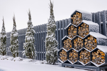 Stacked firewood in hexagonal metal storage covered with snow in a winter backyard.