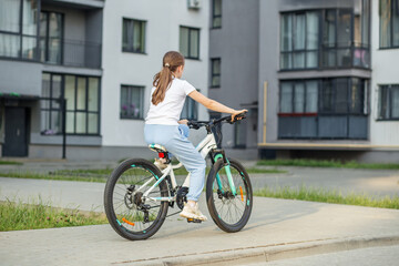 Obraz premium Child rides bicycle on urban pathway near modern apartment complex in bright daylight. Back view