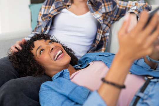 Relaxing on couch, woman laughing while holding tablet, enjoying time with partner