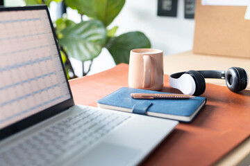 Laptop open on desk with notebook, pen, coffee mug, and headphones nearby