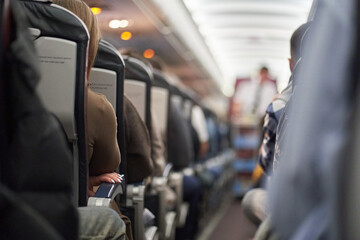 A male steward who distributes food and drinks on board the aircraft. The passengers are sitting in their seats and watching. View along the row. High quality photo