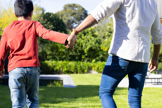 Holding hands, indian father and son walking together in sunny garden