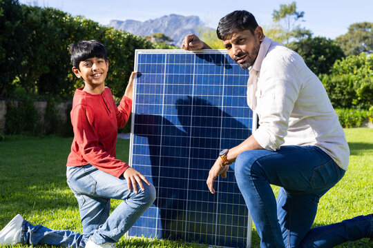 indian father and son installing solar panel together in green garden