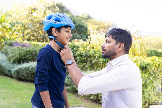 indian father adjusting son's helmet, preparing for outdoor activity in garden - Powered by Adobe