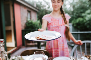 Teenage girl handing over a plate with thinly sliced ham